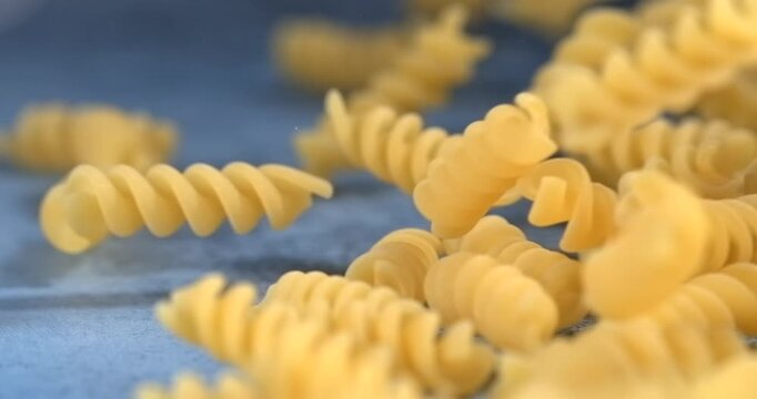 Fusilli pasta falls bounces and rolls across a blue surface in slow motion