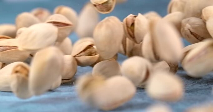 Pistachios fall and bounce across a blue table in slow motion