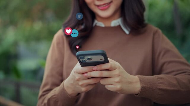 Close up of happy Asian woman holding smartphone with social media icons floating while texting and messaging online app for digital marketing and modern communication lifestyle.