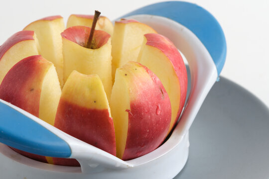 Fresh red apple sliced into neat wedges using blue and white plastic apple corer cutter.