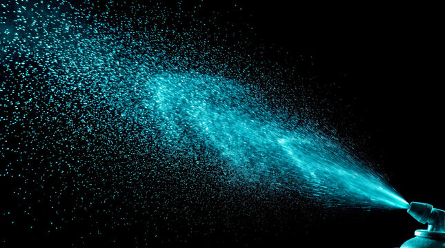 Close-up of glowing blue paint particles spraying in dark background for creative visual effects