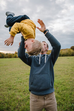 Dad throwing and turning little boy while son playing with dad outdoors in autumn field. Father and son having fun together during a walk in nature.