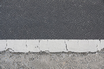 Fototapeta premium Cracked Asphalt Road Lane Marker. Worn highway boundary line evokes themes of aging infrastructure and resilience while separating textured ground surfaces outdoors.
