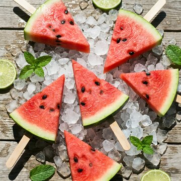 Sliced watermelon on sticks served over crushed ice with lime wedges and mint leaves on a rustic wooden table refreshing summer treat