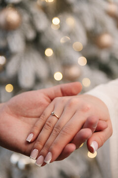 Close-up of a marriage proposal, man holding woman's hand wearing a diamond engagement ring. Festive blurred background with bokeh lights. Romantic moment, love, engagement, promise.