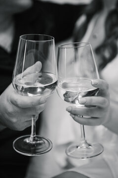 Cheers. Toast closeup. A romantic close-up of a man's and a woman's hands clinking glasses of white wine. Wedding morning or celebration. Soft focus background. Black and white photo.