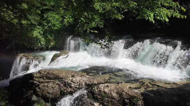 Cascading waterfall at Martvili canyon, rushing water over rocky ledges, lush forest scenery, peaceful nature, Georgia travel landscape