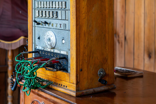 Vintage wooden telephone switchboard station with metal control panel, numbered buttons, toggle switches, and a tangled mess of green and red patch cords with jacks attached to the front.