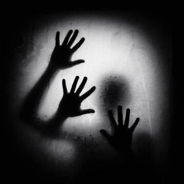 Eerie black and white showing human hand silhouettes pressed against a wet, foggy glass surface, creating a ghostly and mysterious atmosphere of entrapment and fear
