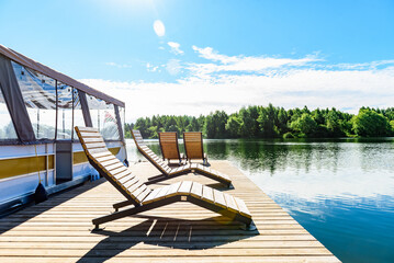 A pontoon boat is moored to a wooden dock for relaxation by the tranquil waters surrounded by green trees. © Natallia