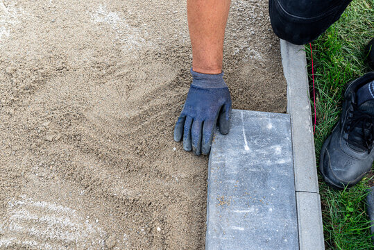 Worker using glove laying paving slab on sand base