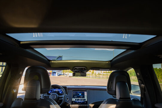 Panoramic sunroof and front dashboard view inside a modern luxury car cabin with sun flare, close up.