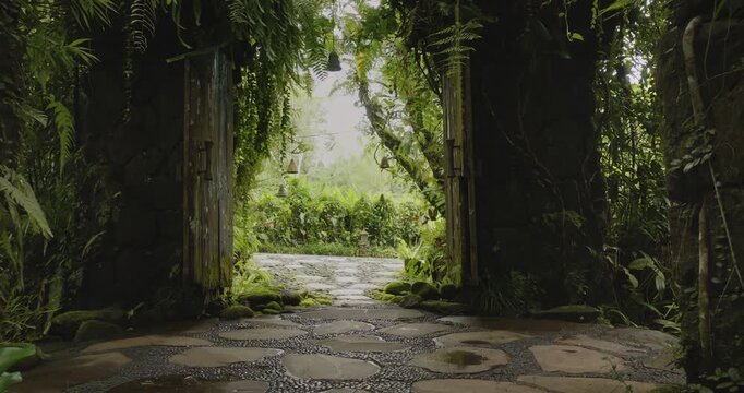 Jungle Ubud stone gate entrance with wooden doors leading to a lush tropical garden path on Bali island, surrounded by vibrant green foliage and ancient mossy walls. Explore remote travel destinations