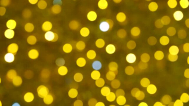 Close-up out-of-focus background covered in golden-yellow glitter. Bokeh effect with circular glowing light orbs. Rhythmic flickering pattern with intensity shifts and occasional blue color changes