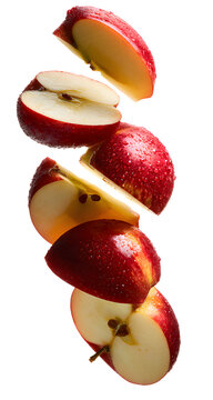 A group of fresh red apple pieces falling through the air with water droplets on the skin, captured in a high speed motion.