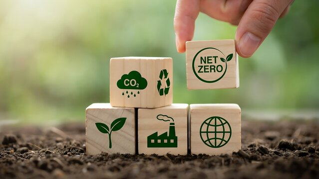 Hand placing wooden cube with net zero icon on top of other cubes with eco symbols, symbolizing carbon neutral goal, sustainability, and environmental responsibility.