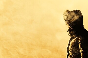 Naklejka premium Close-up of a person in a winter jacket with fur hood covered in snow against a textured golden background
