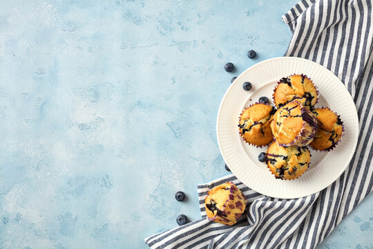 Tasty blueberry muffins on plate with striped napkin and copy space