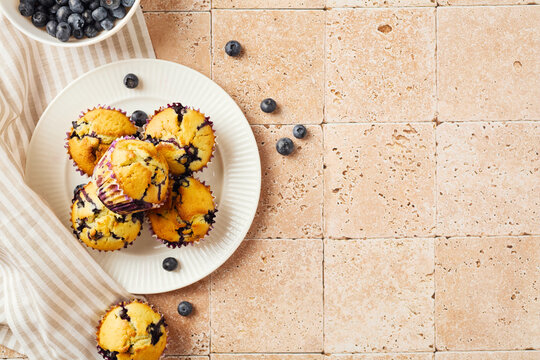 Fresh blueberry muffins on white plate over beige tile background