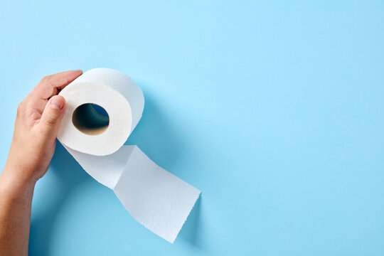 Hand holding roll of toilet paper on blue background with space