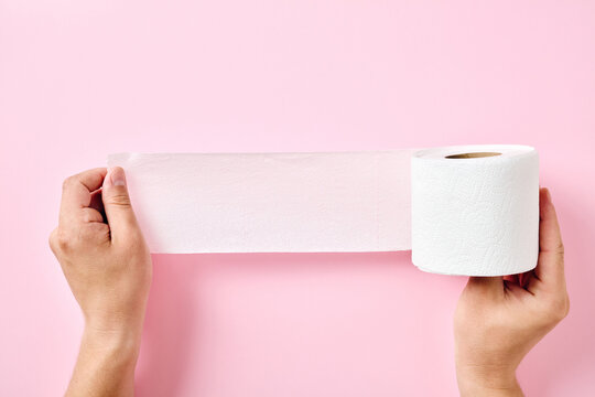 Two hands stretching open toilet paper roll on pink background