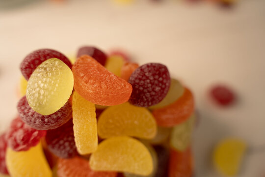 closeup macro of assorted sugar-coated gumdrops and jelly candies piled on a tabletop surface under warm studio lighting, soft-focus shallow depth with bright yellow, orange and red glossy textures