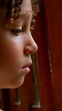 Vertical video: Boy in profile reacting to warm light, blinking and shedding tear at wooden window