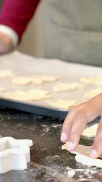 Vertical video: Pressing cutter into dough apron hands lifting cuts placing cookies on pan to bake