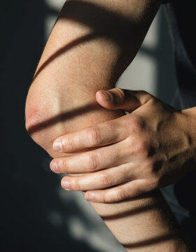 Close up hand elbow pain joint injury skin adult human health discomfort holding arm ache medical problem muscle physical therapy stress tension male person shadow sunlight indoors care touch