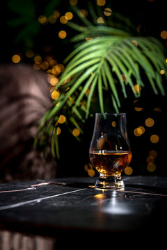 Aromatic scotch whisky in glencairn glass under green palm leaf on black table. Sophisticated alcohol beverage degustation, luxury bourbon, brandy or rum in dark lounge.