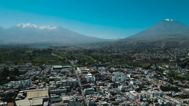 Panoramic drone shot flying over Arequipa city showcasing the stunning snow-capped Chachani and Misti volcanoes.