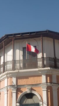 Slow motion shot of the red and white Peruvian flag fluttering from a balcony of an ancient building.
