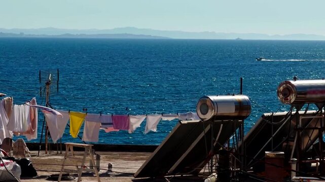 Solar Water Heater Panels And Laundry Clothesline On Rooftop Overlooking Blue Sea Waters. Sunny Day Coastal 
