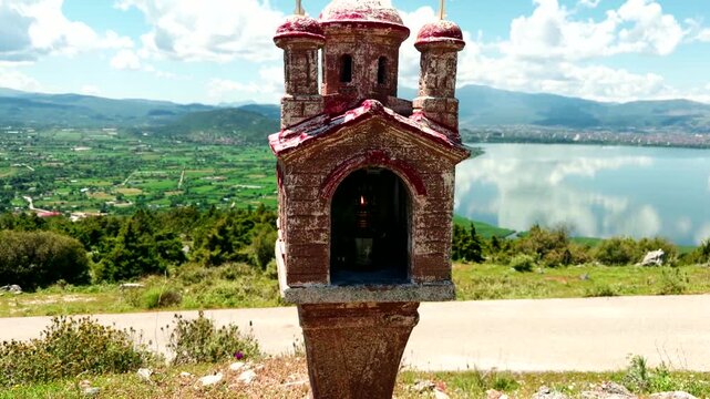 Small Orthodox Roadside Shrine Monument With Lit Candle Overlooking Scenic Lake. Religion Concept Greece