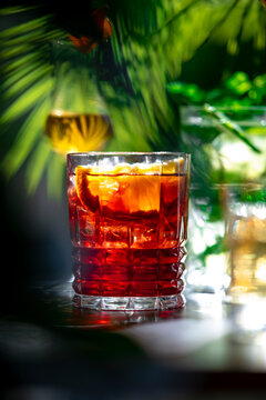 Beautiful summer cocktails selection features alcoholic drinks like bittersweet Negroni inside textured glass. Sophisticated nighttime aesthetic, creative bar lighting, premium nightlife vibes.