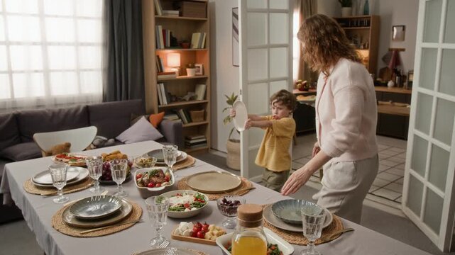 Caucasian mother and young sons setting dining table with healthy food at home. Clip for family lifestyle commercials, holiday dinner promotions, or home cooking advertisements