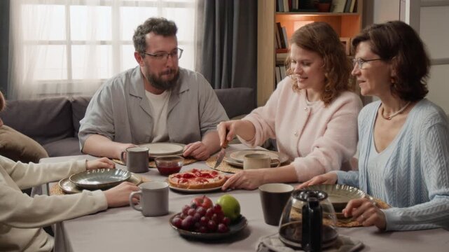 Multigenerational Caucasian family sitting at dining table with woman slicing homemade pie. Clip for food delivery ads and family lifestyle marketing