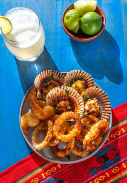Peruvian hot seafood appetizers platter with parmesan scallops, fried calamari and Pisco Sour drink