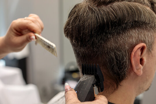 Barber using an electric hair clipper with a hair comb to cut a man hair, creating a professional fade haircut in a modern barbershop salon this quiet afternoon