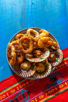 Peruvian hot seafood appetizers platter with parmesan scallops, fried calamari and Pisco Sour drink