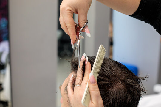 Barber using scissors and a comb to cut a man hair at the back of the head, professional hair cutting technique performed in a busy barbershop hair salon today afternoon