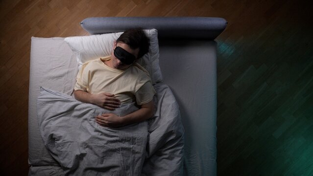 Man sleeping peacefully in bed at night wearing a black eye mask for deep rest and tranquility, promoting good sleep hygiene and overall wellness