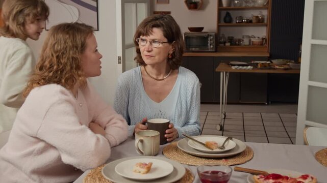 Middle aged Caucasian woman and young Caucasian woman talking at dining table during family dinner. Clip for marketing campaigns for multigenerational living or family insurance