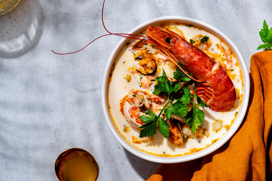Creamy seafood chowder soup with jumbo prawn, mussels in bowl on table with napkin. Close up gourmet seafood menu background, luxury restaurant delicacy concept.