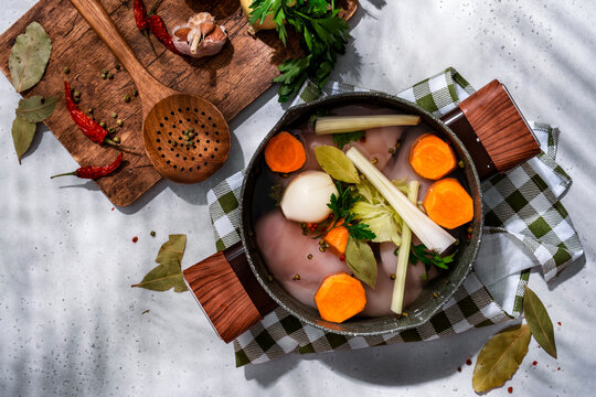 Raw chicken soup broth preparation. Traditional home cooking recipe with roots, herbs, and wooden board.