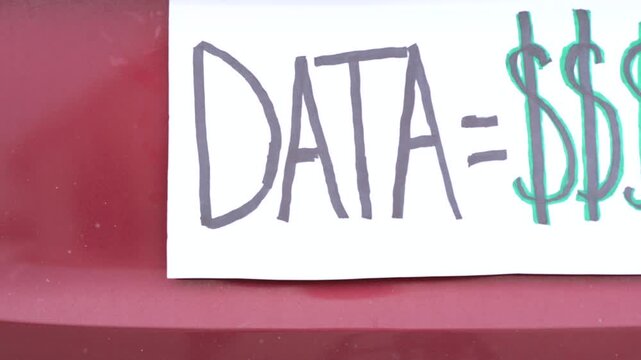 Handmade sign on car license plate slot messages like Opt Out and Data equals money to protest ALPR vehicle surveillance and Fourth Amendment rights