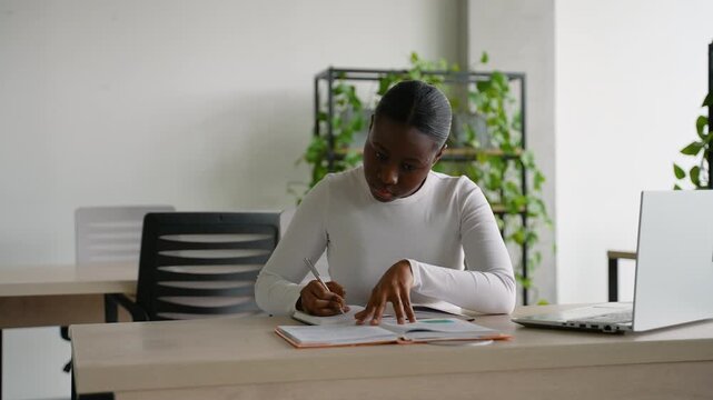 Focused african american woman writing in a notebook at her desk