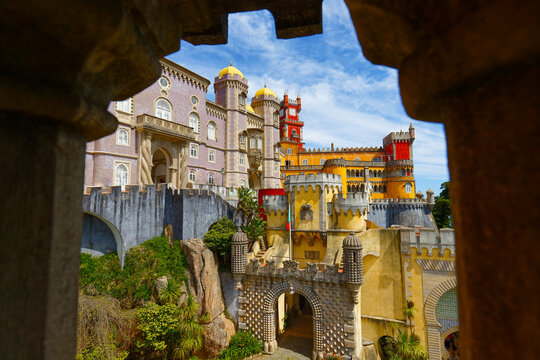 Breathtaking panoramic view of the Pena Palace in Sintra through a crenellated stone window .