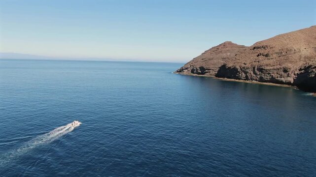 Amazing aerial view of a motorboat sailing in the calm blue Atlantic Ocean near the volcanic coastline of Gran Canaria, Spain