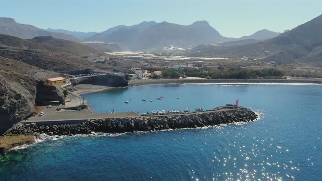 Picturesque aerial view of the Charco de La Aldea port, showing boats in the clear blue water with the mountains in the background